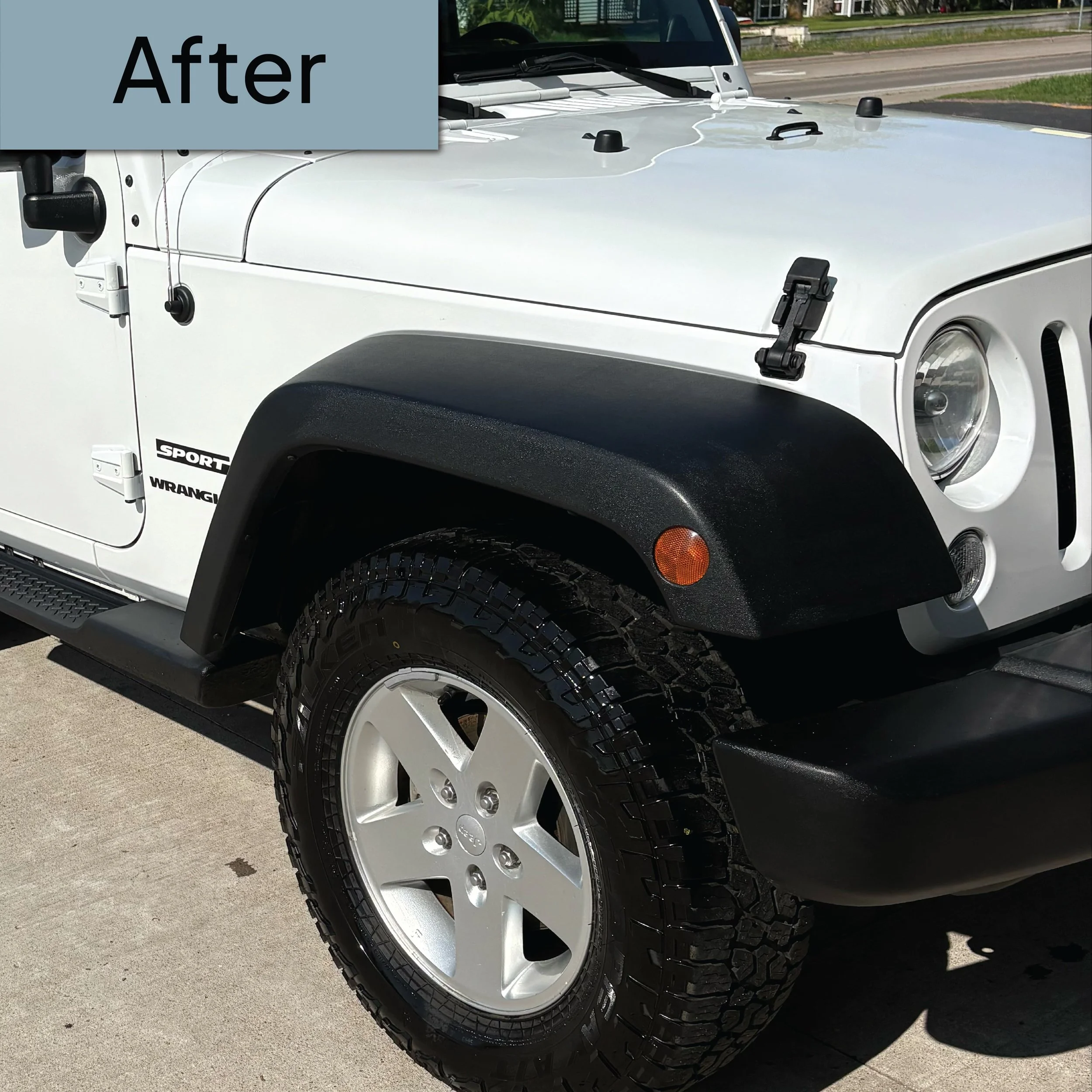 Close-up of the front part of a white Jeep Wrangler Sport with large off-road tires, black fender flares, and black side mirrors parked on a concrete surface.