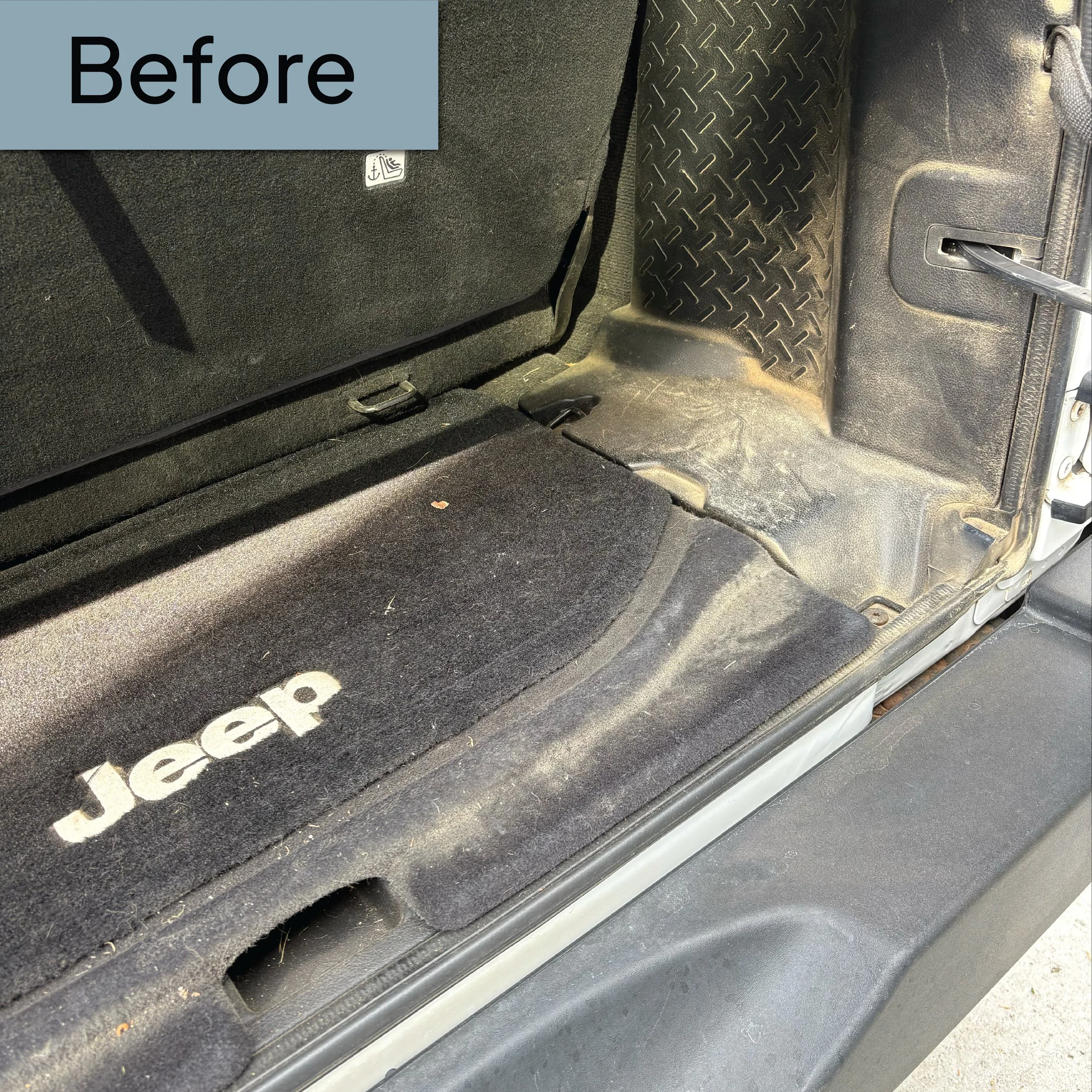 The back interior of a vehicle showing the rear seat, a rubber mat with a diamond pattern, and part of a door with a mesh pocket and handle.