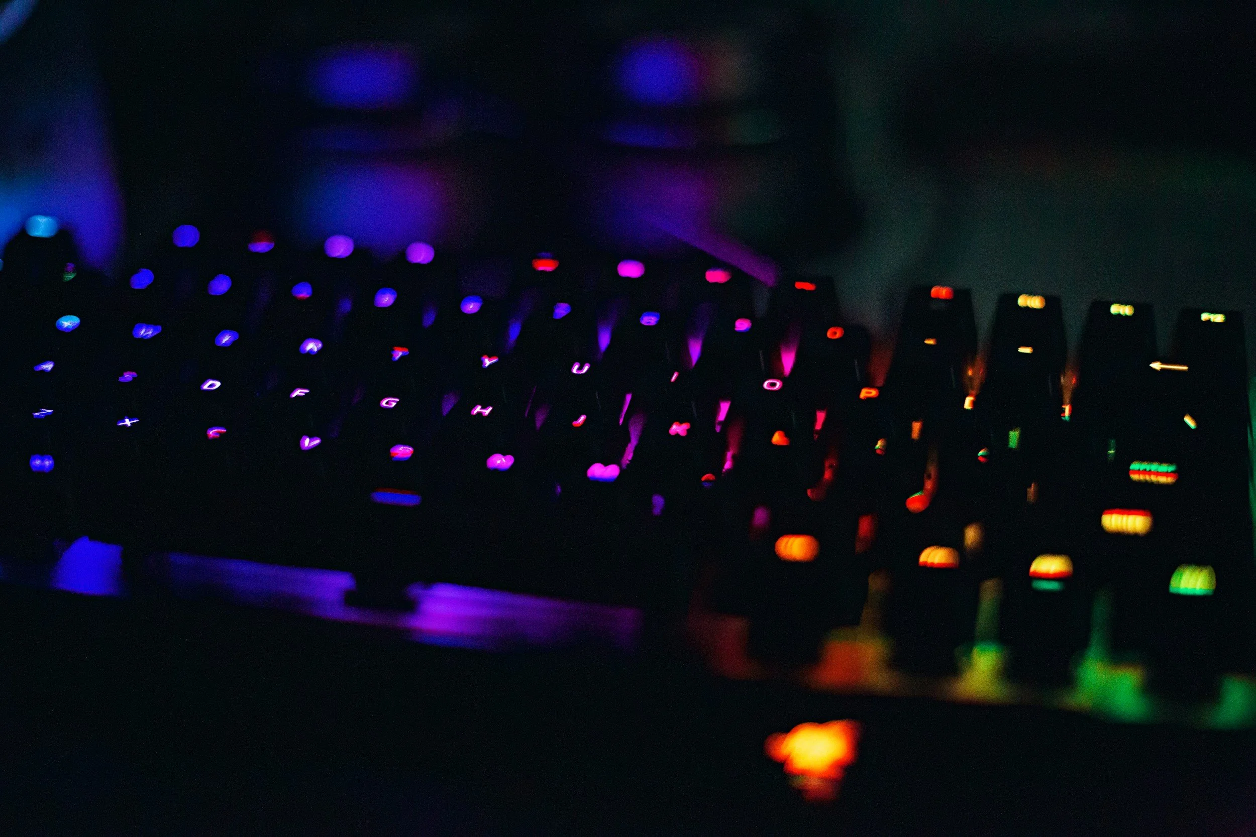 A computer keyboard with multicolored backlit keys in a dark environment.