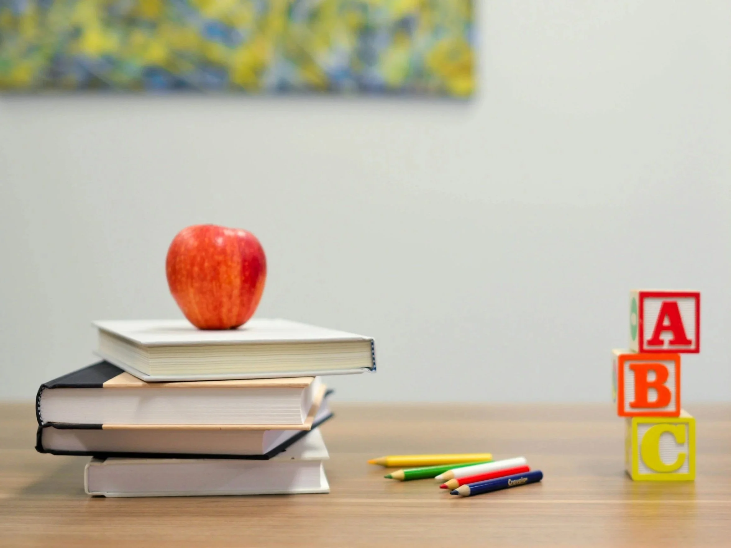 Image of a table with books, pencils, an apple, and ABC blocks