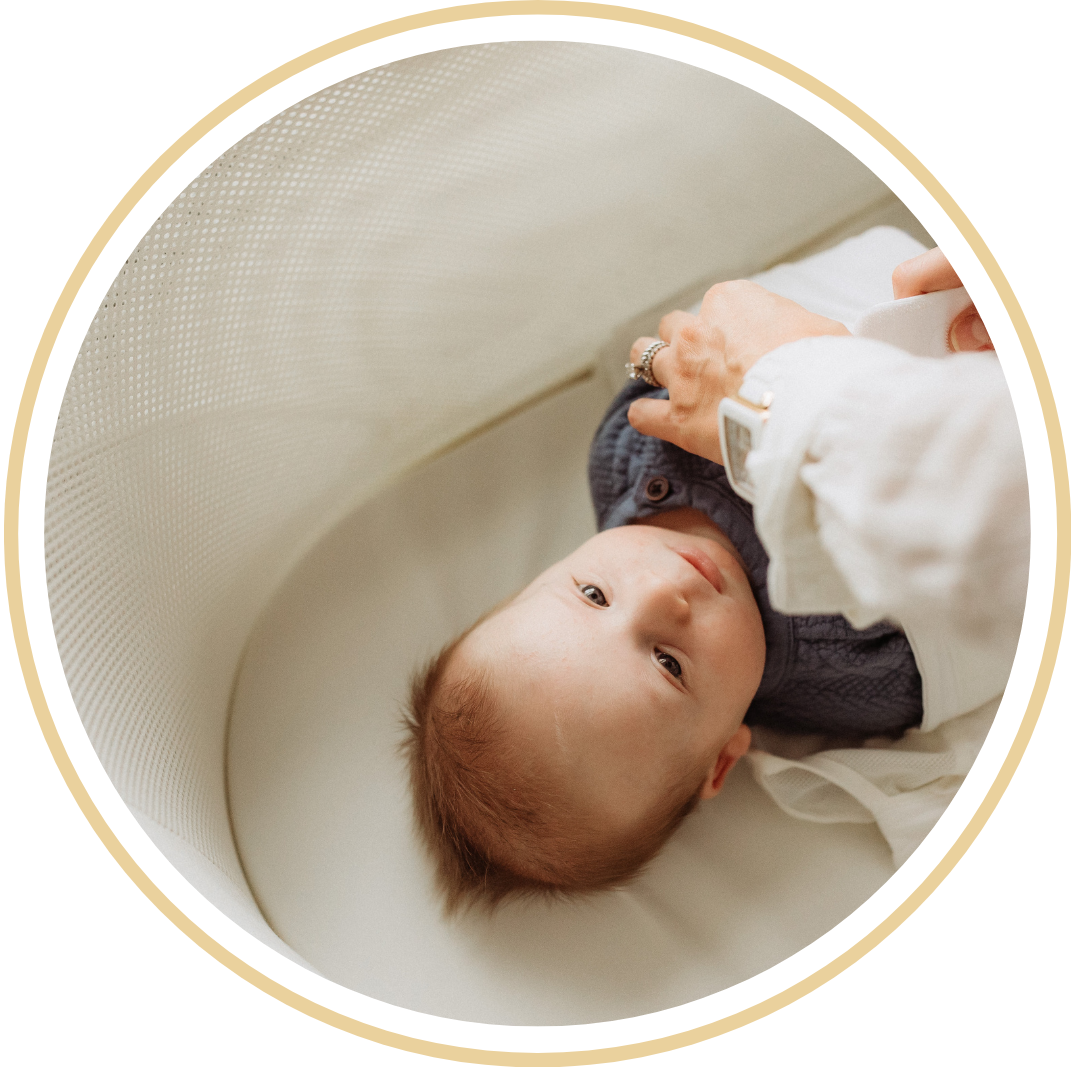 A mother practicing responsive sleep support by placing a gentle hand on her baby’s chest in a sunlit, boutique-style nursery. in Lakewood