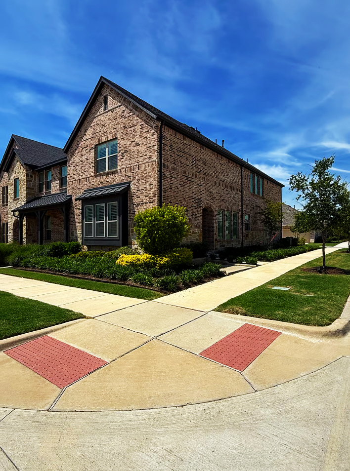 A two-story brick house with a manicured lawn, sidewalk, and a blue sky.