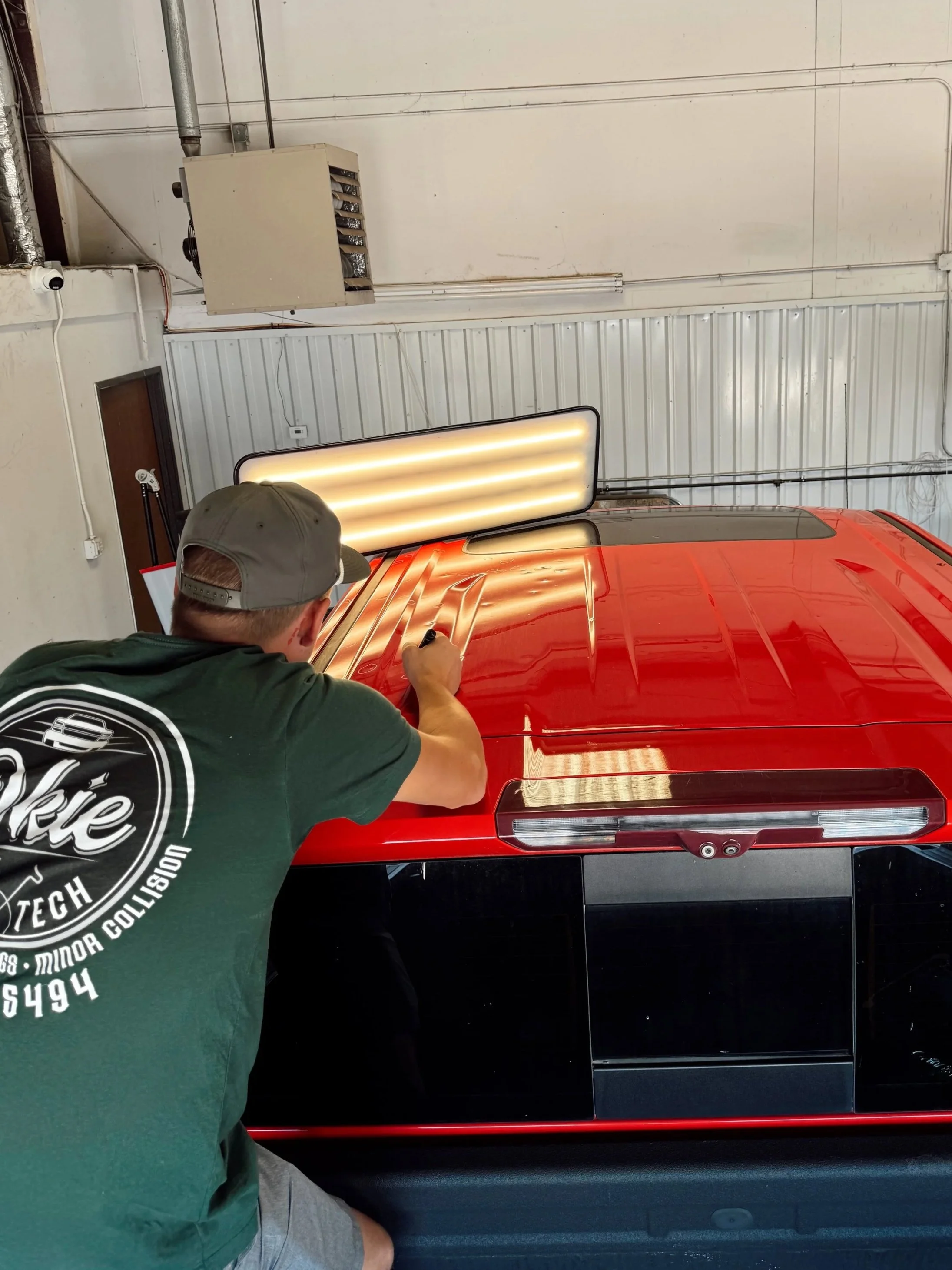 A man in a green T-shirt and gray cap signs a red and black vehicle inside a garage.