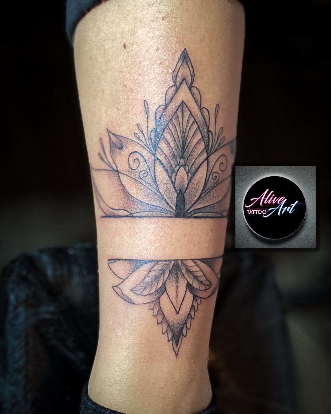 A black ink geometric floral tattoo on a person's forearm, featuring symmetrical leaf and petal patterns with a faint, intricate design.