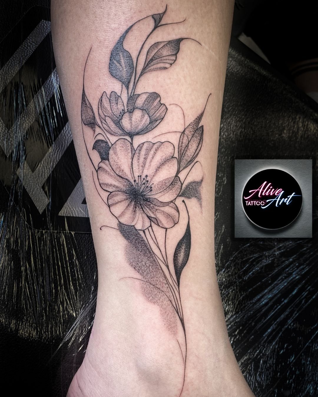 Black and gray floral tattoo on person's leg featuring large open flowers, leaves, and delicate line work.