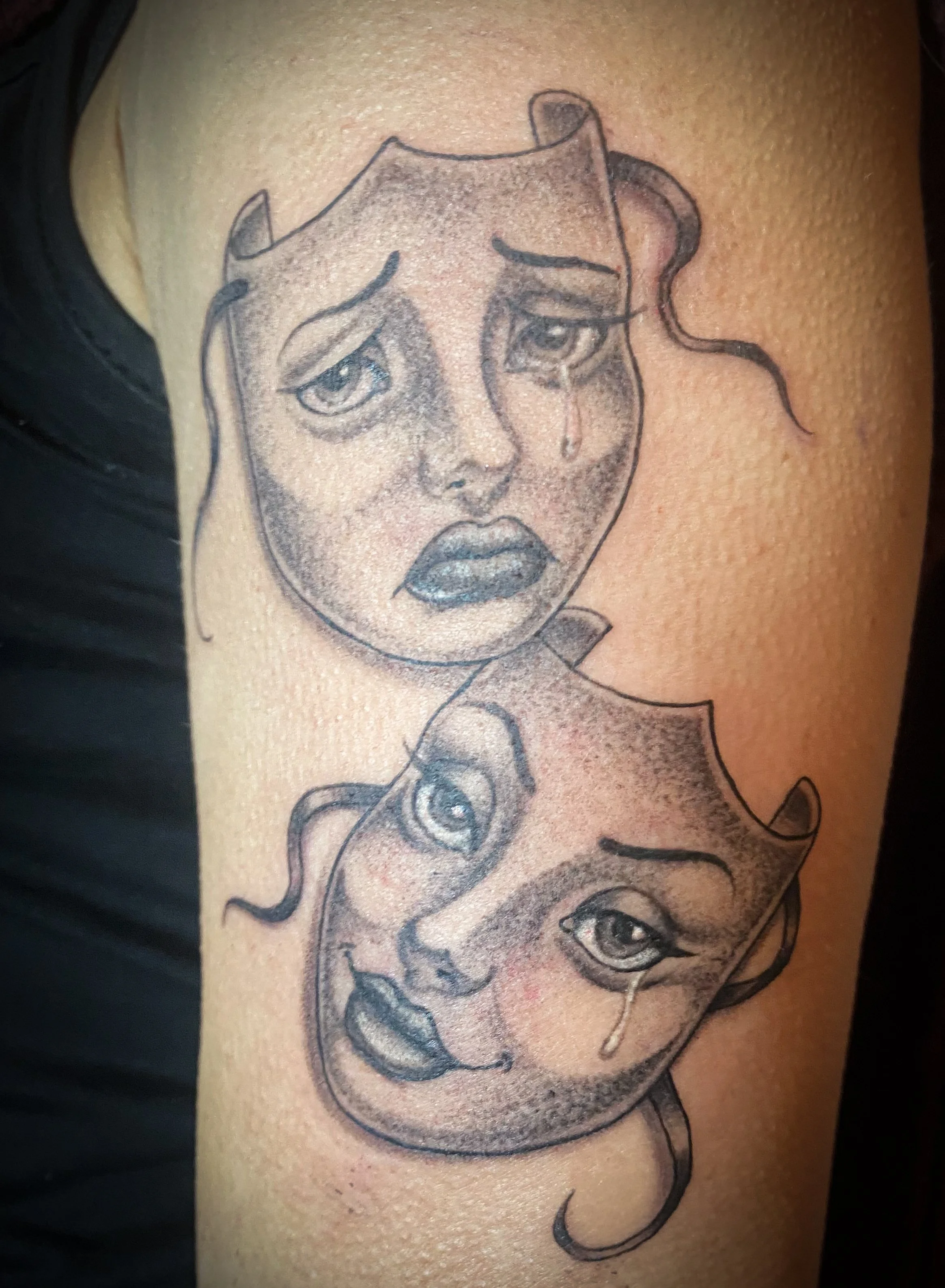 Tattoo of two crying faces, one above the other, with expressive eyes and tears, outlined in black ink on skin.