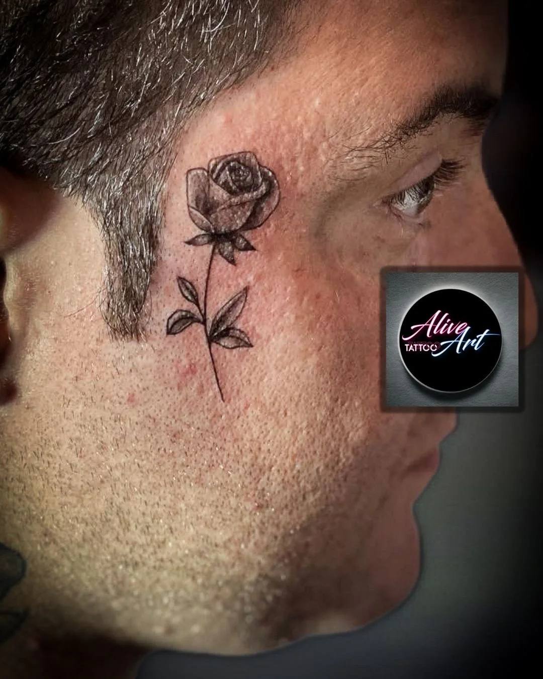 Close-up of a person's face with a black and gray rose tattoo on the cheek near the eye.