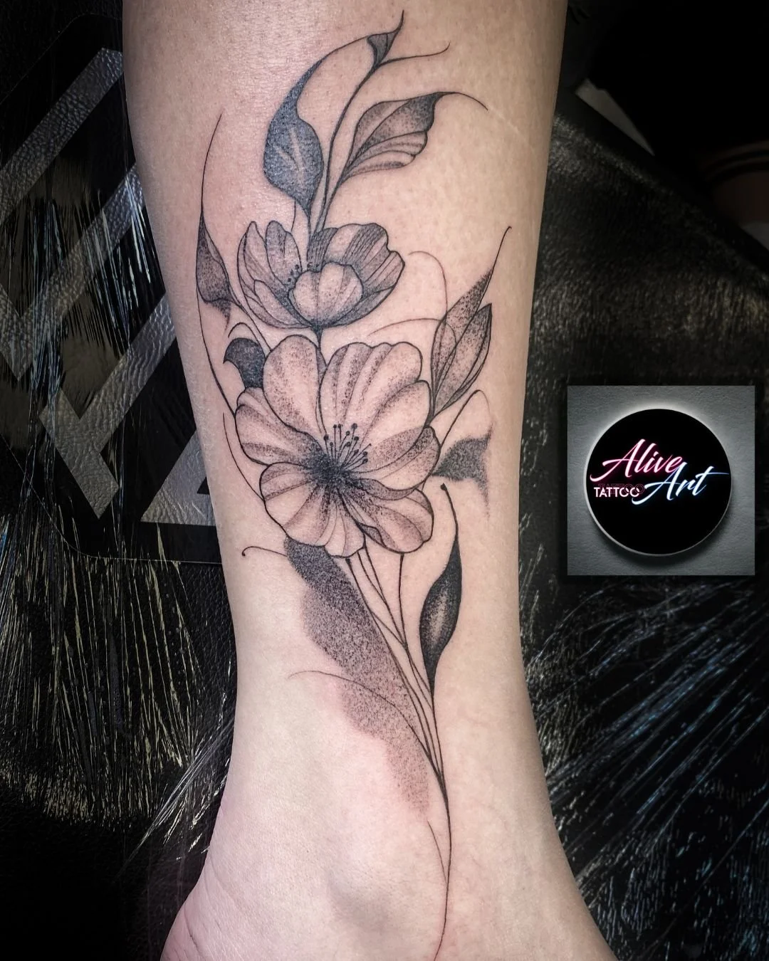 Black and gray floral tattoo with large blooming flowers, leaves, and delicate linework on a person's forearm.