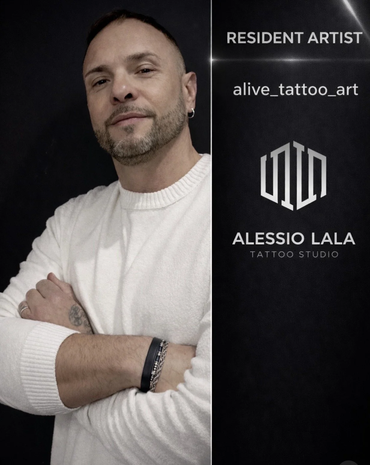 Portrait of a man with short brown hair and a beard, wearing a white sweater, crossing his arms with tattoos and bracelets visible, standing next to a black sign with white text for Alessio Lala Tattoo Studio, including their Instagram handle and logo.
