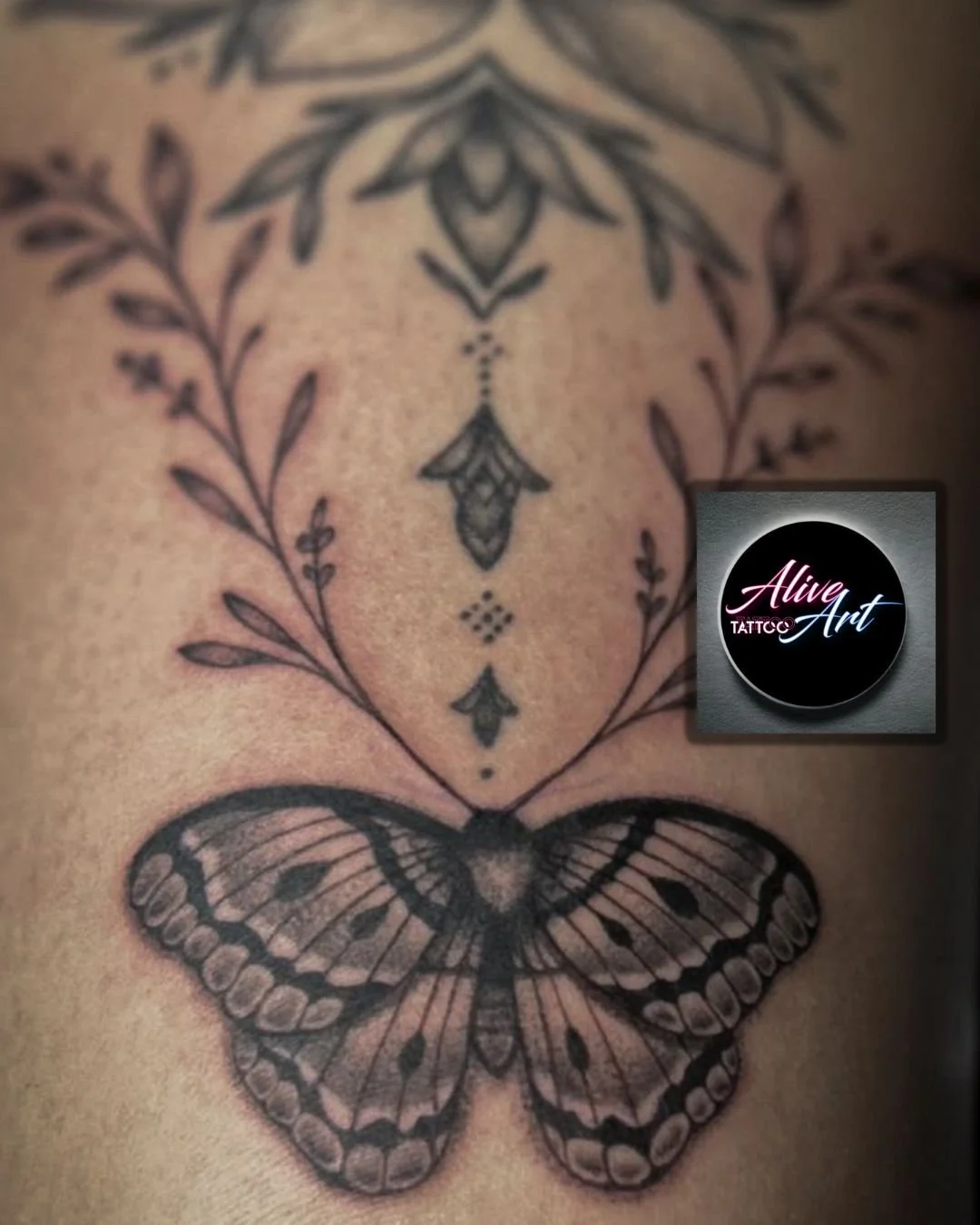 Tattoo of a butterfly below a decorative, floral line design on skin