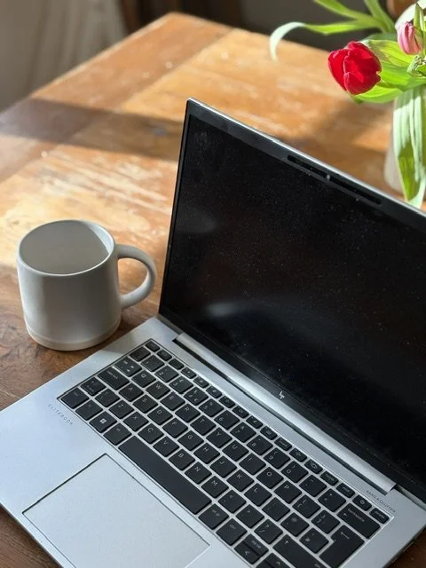 Open laptop with black screen, white coffee mug, and a vase of red tulips on a wooden table.