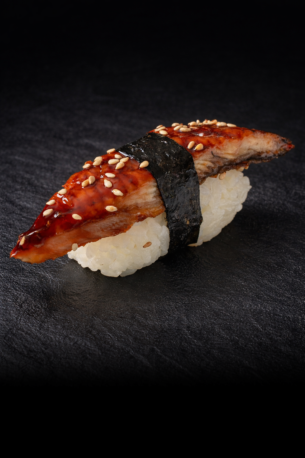 A piece of sushi topped with glazed eel, sesame seeds, and wrapped with nori seaweed on a bed of rice.