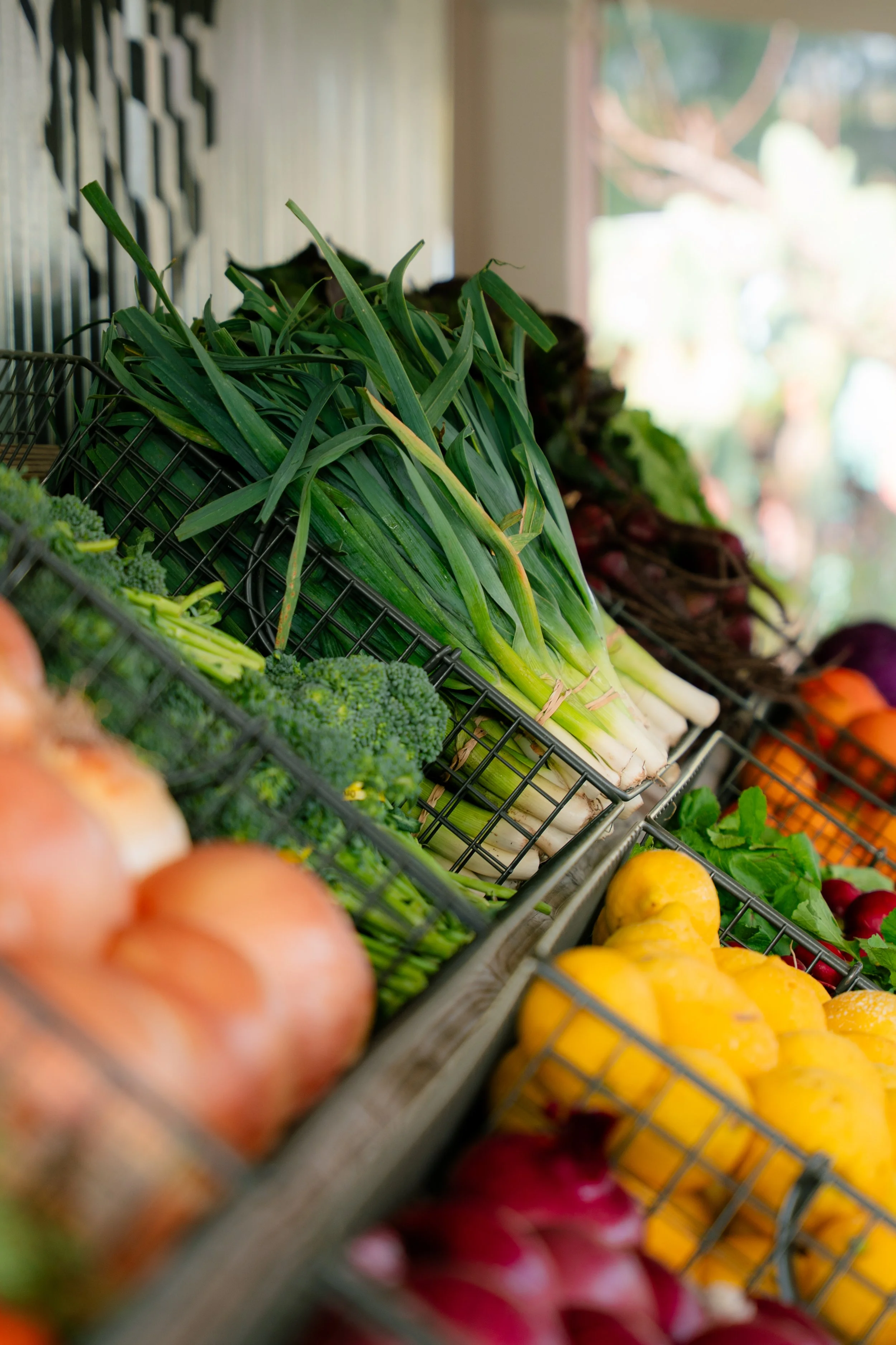 Fresh vegetables including green onions, broccoli, and yellow peppers displayed in a market or grocery store.