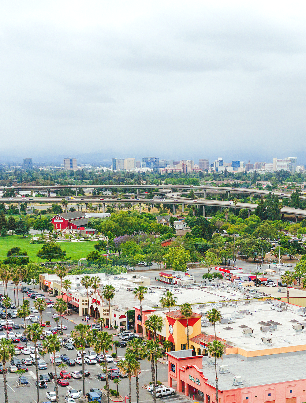 Aerial view of a suburban neighborhood with houses, trees, and streets, and a large parking lot in the lower part of the image.
