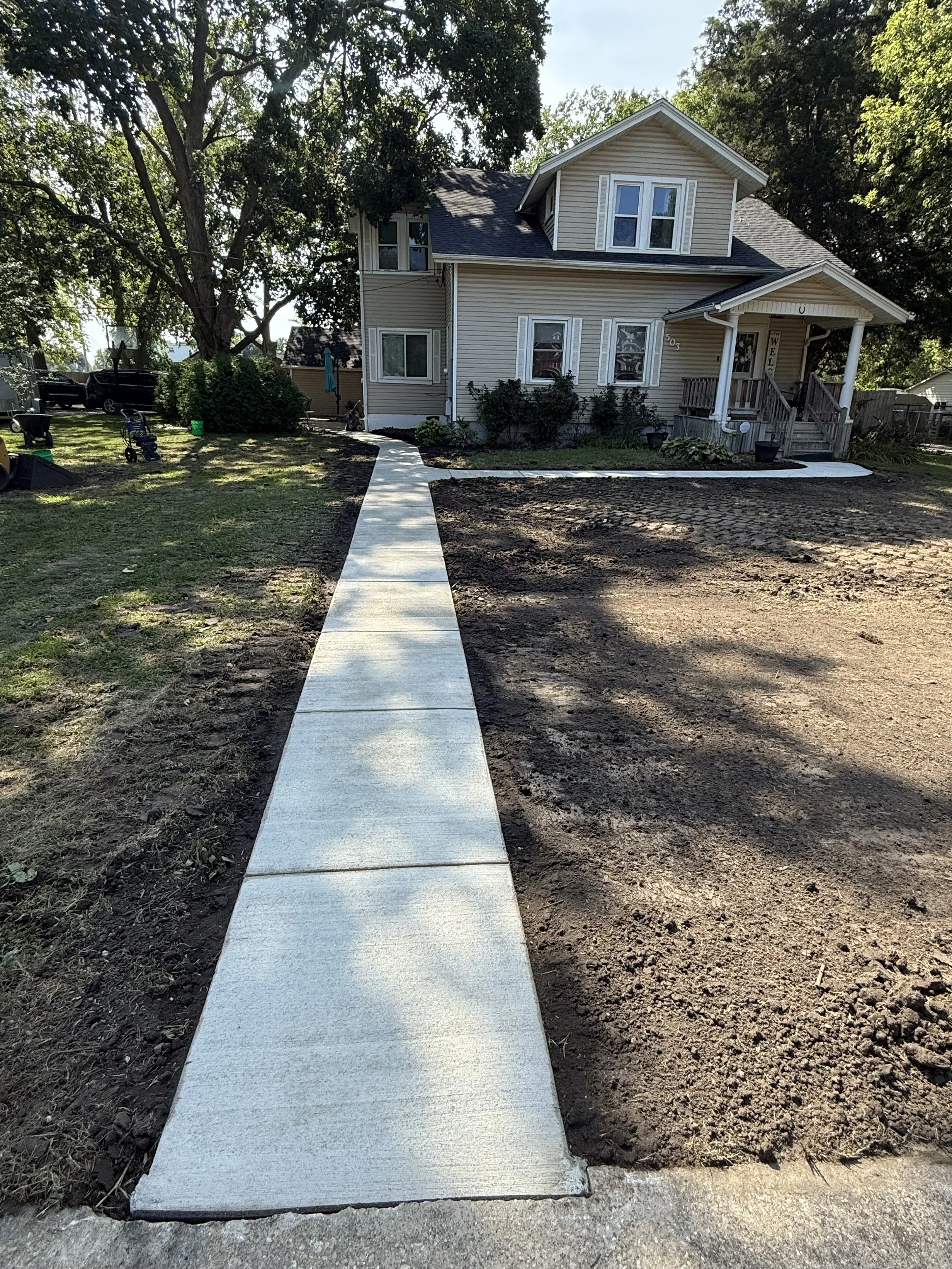 A newly poured concrete sidewalk leading to a house with a small front porch.