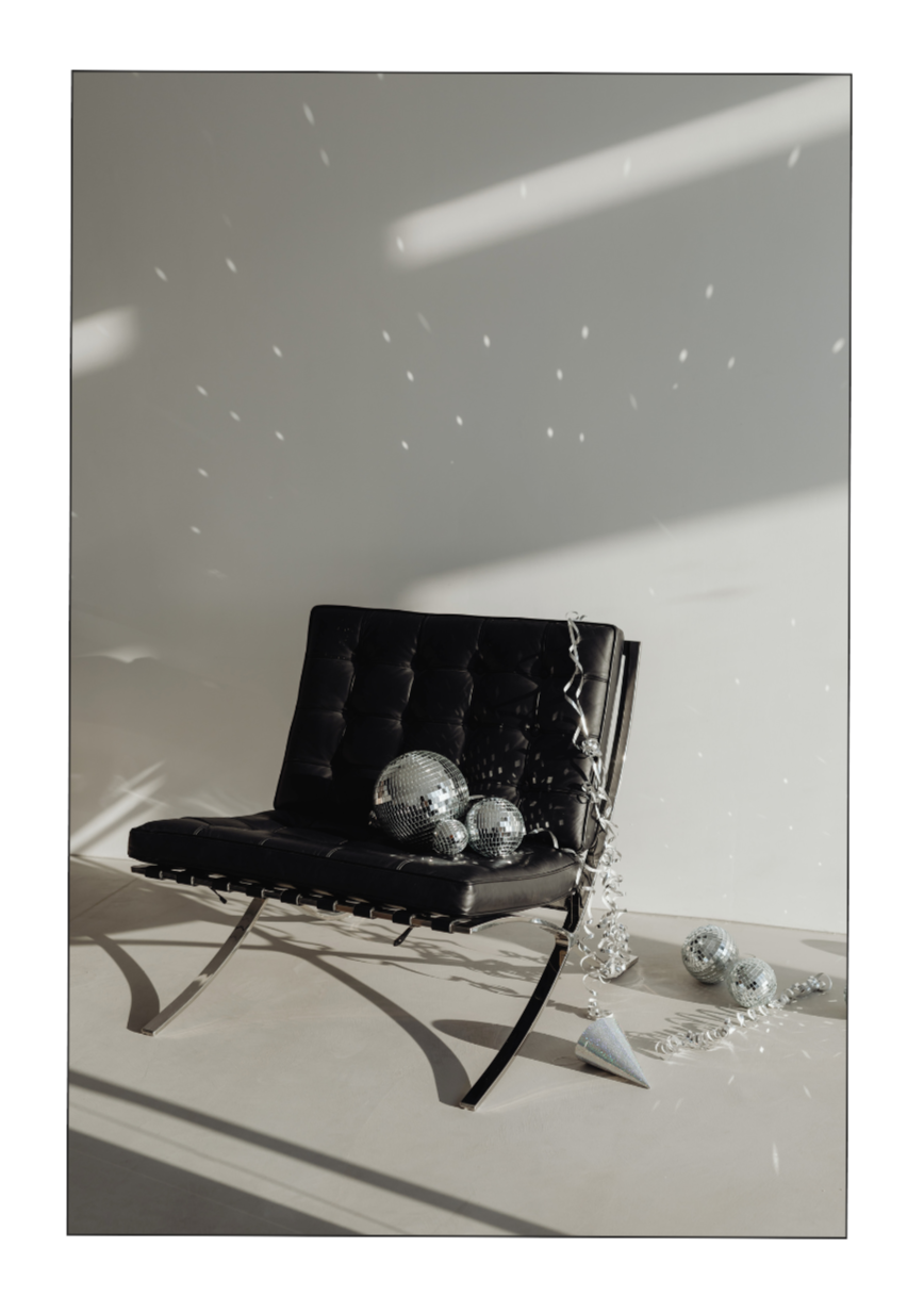 Ein schwarzes Leder-Sitzmöbel mit Metallrahmen, dekoriert mit Disco-Kugeln und Party-Dekorationen, auf einem hellen Boden vor einer weißen Wand mit Lichtreflexen.