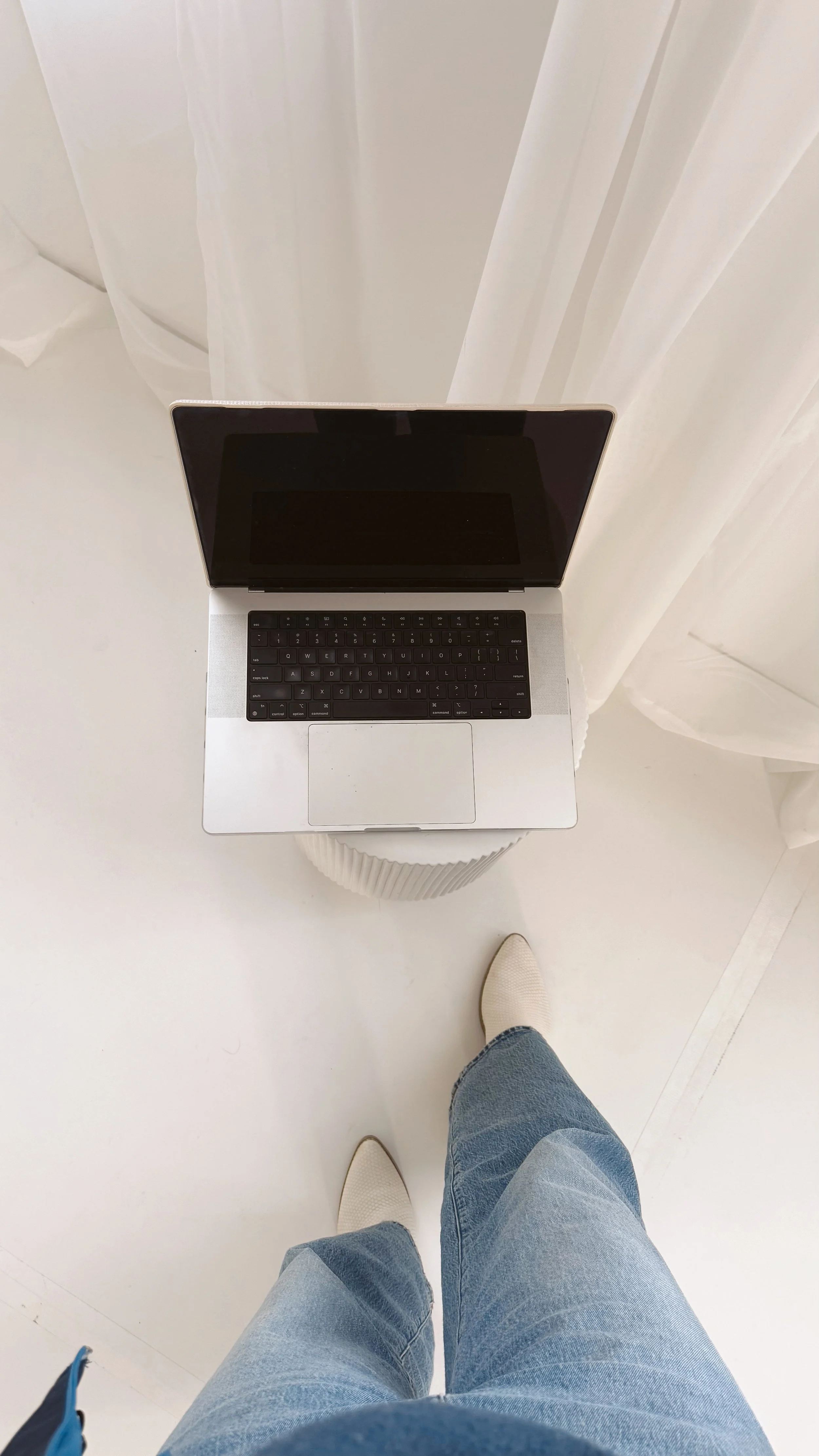 Ein oberes Foto zeigt einen Laptop auf einem runden, weißen Tisch, während die Person, die die Kamera aufgenommen hat, Jeans und weiße Schuhe trägt.