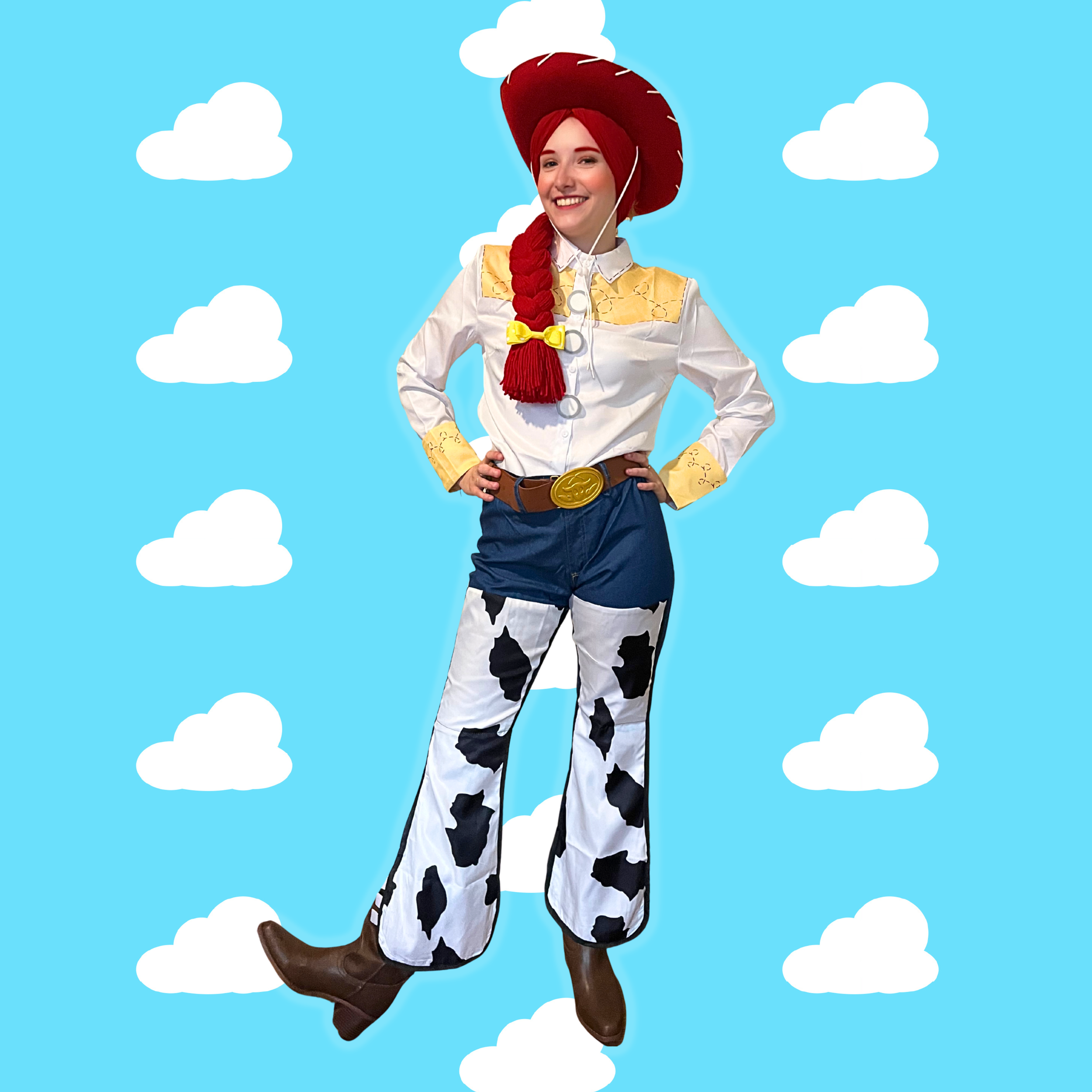 Person dressed as Jessie from Toy Story, wearing a cowboy hat, white shirt with yellow yoke, cow-print pants, and brown boots, standing with hands on hips against a backdrop of blue sky with white clouds.