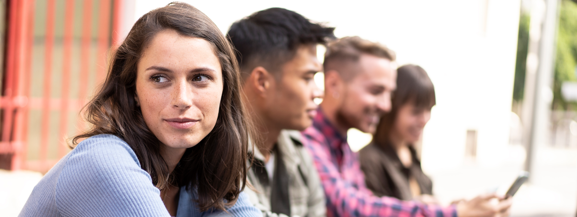 Group of young students sitting outdoors, with the woman in the foreground looking to the side, smiling softly.