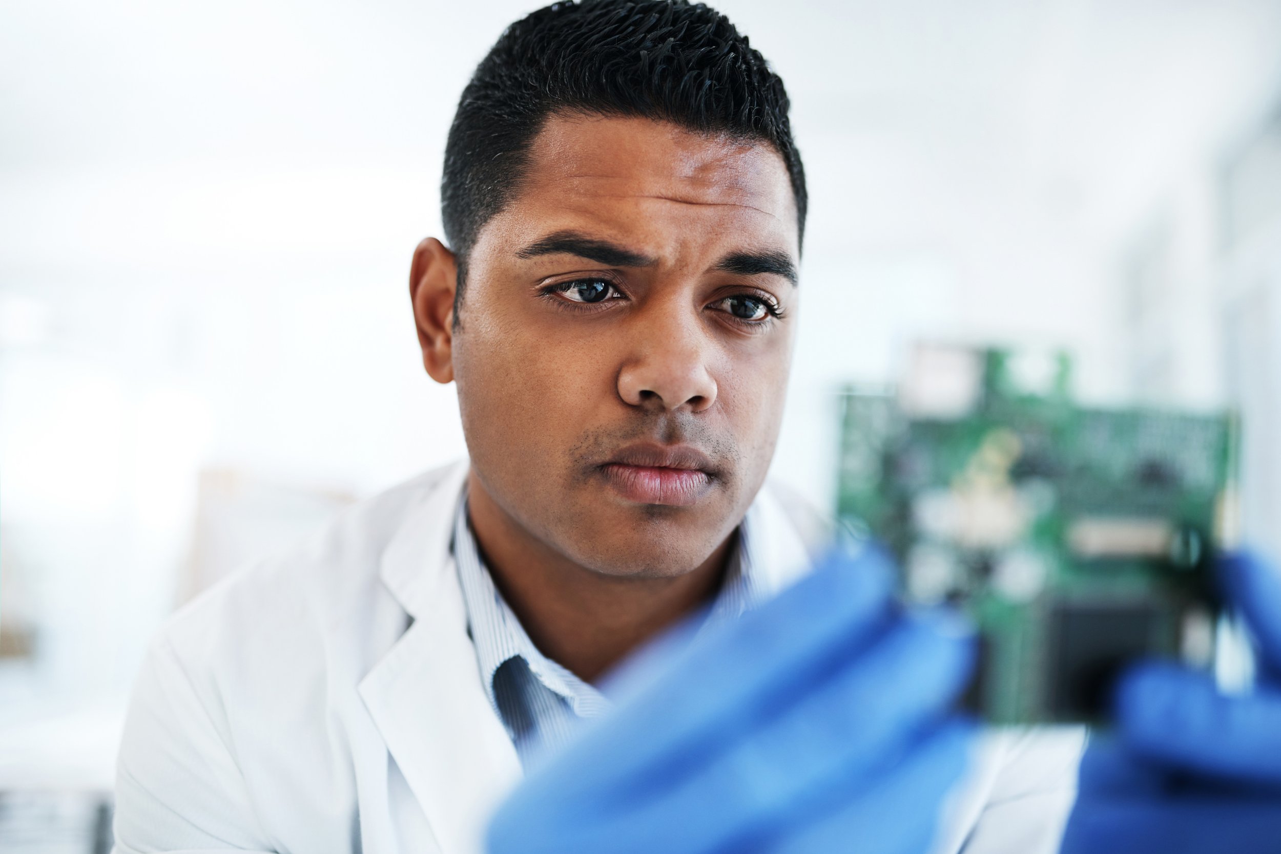 A young student in a white lab coat looking at a computer motherboard in a laboratory setting.