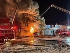Firefighters battling a fire at night, with flames and smoke coming from a building, and fire trucks present.