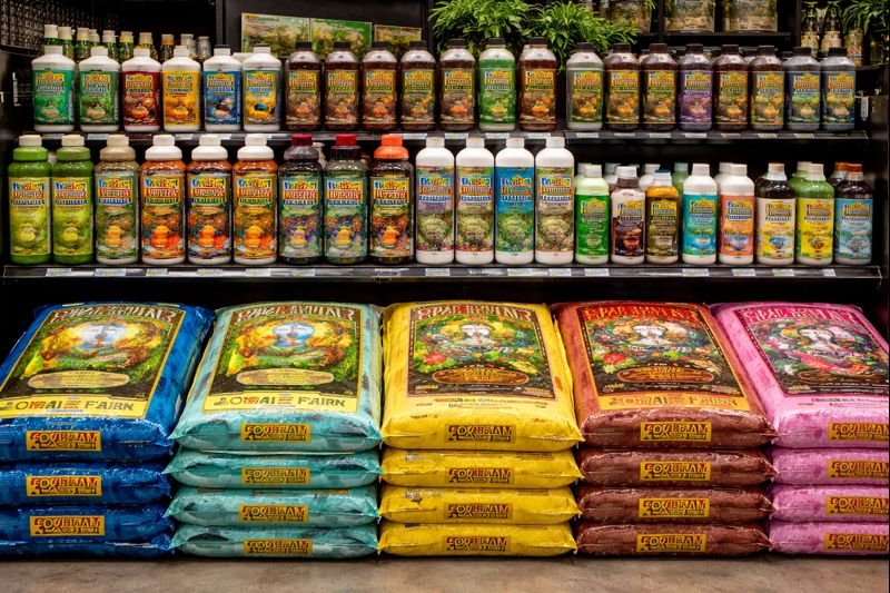 Display of various gardening products, including bottles of plant fertilizer and bags of potting soil, on store shelves.