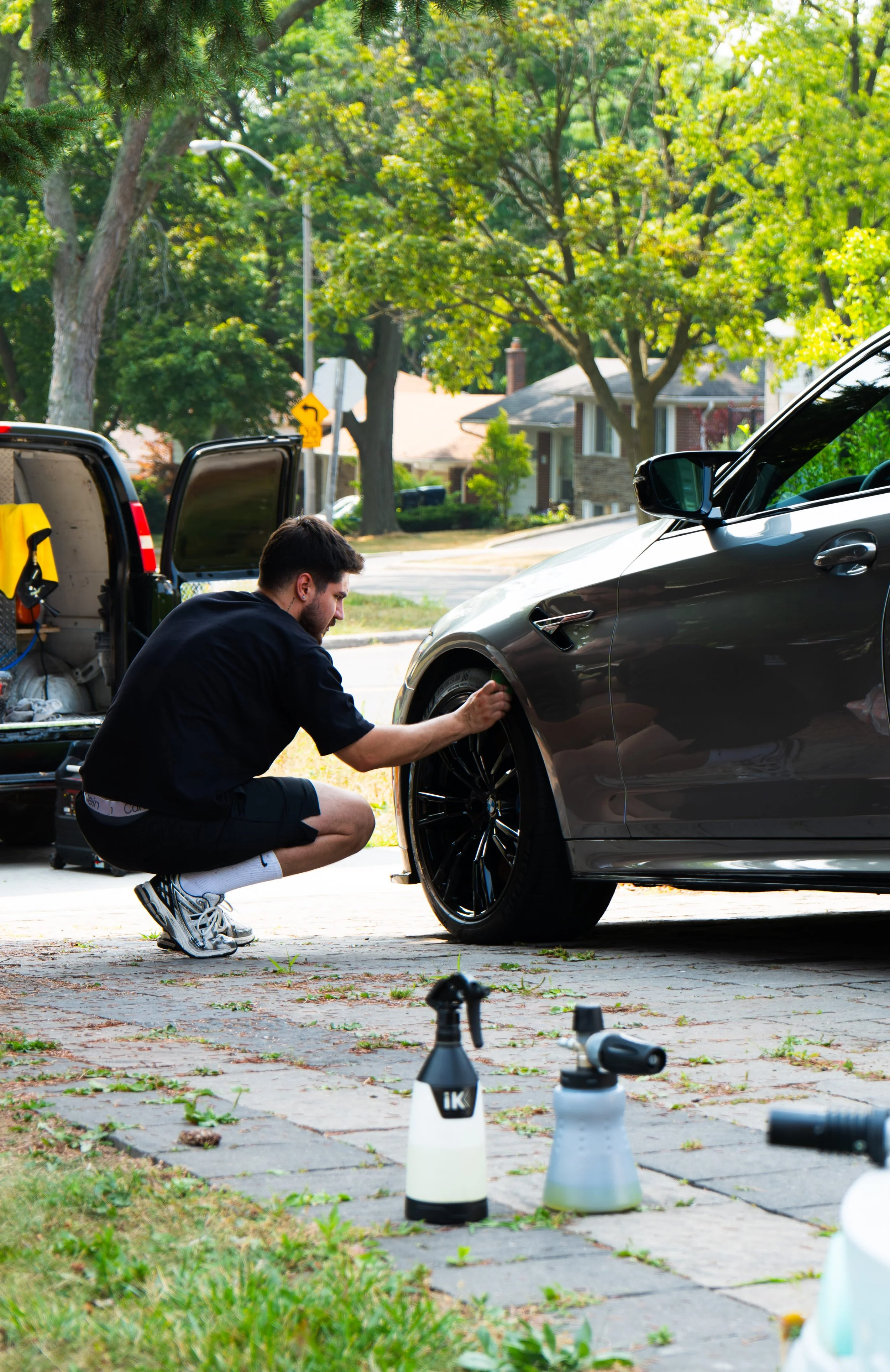 Mobile car detailing service cleaning alloy wheels on a sports car at a residential location.