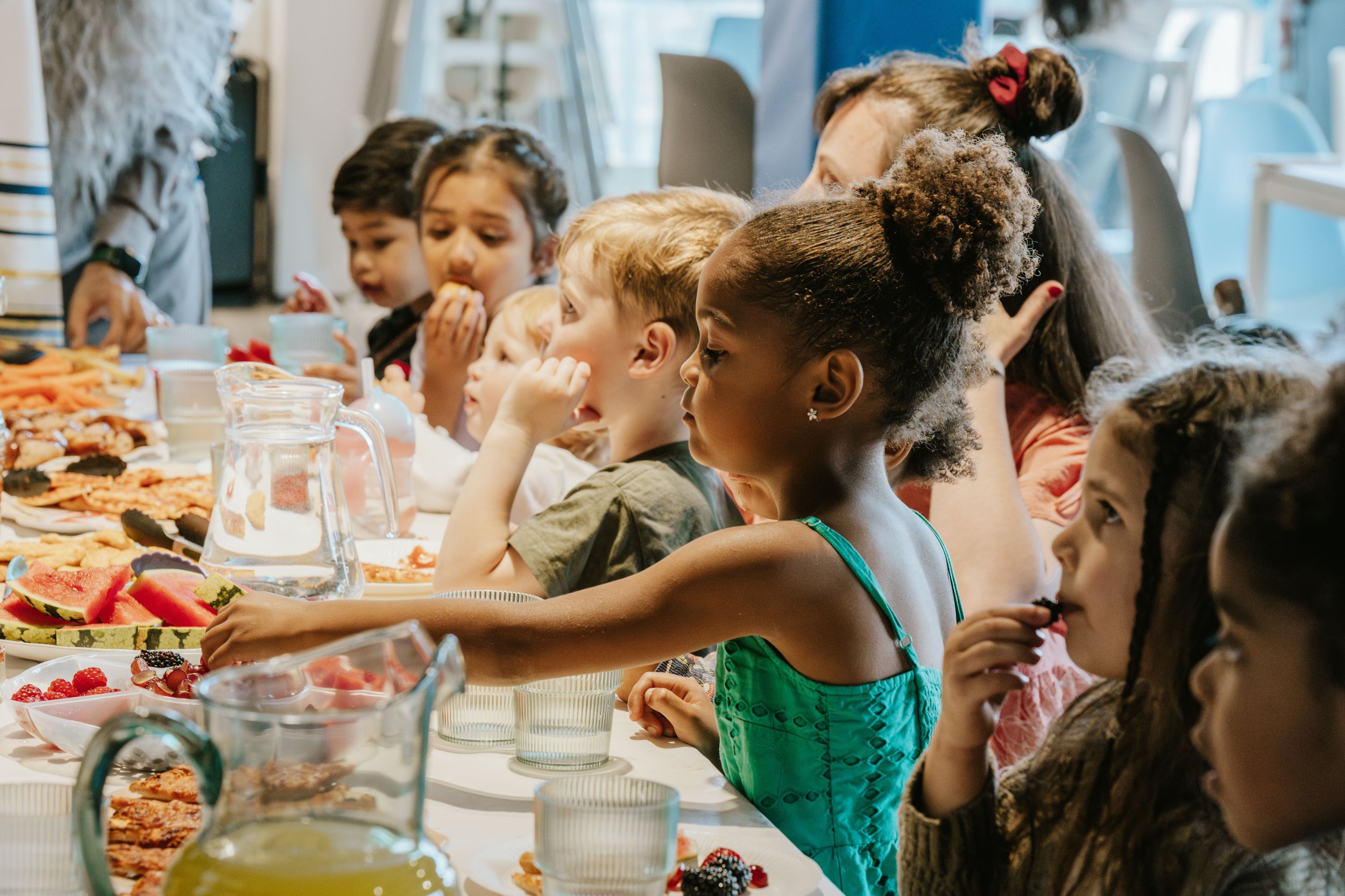 Children sitting at a table with various desserts and fruit, engaged in eating during a gathering or celebration.