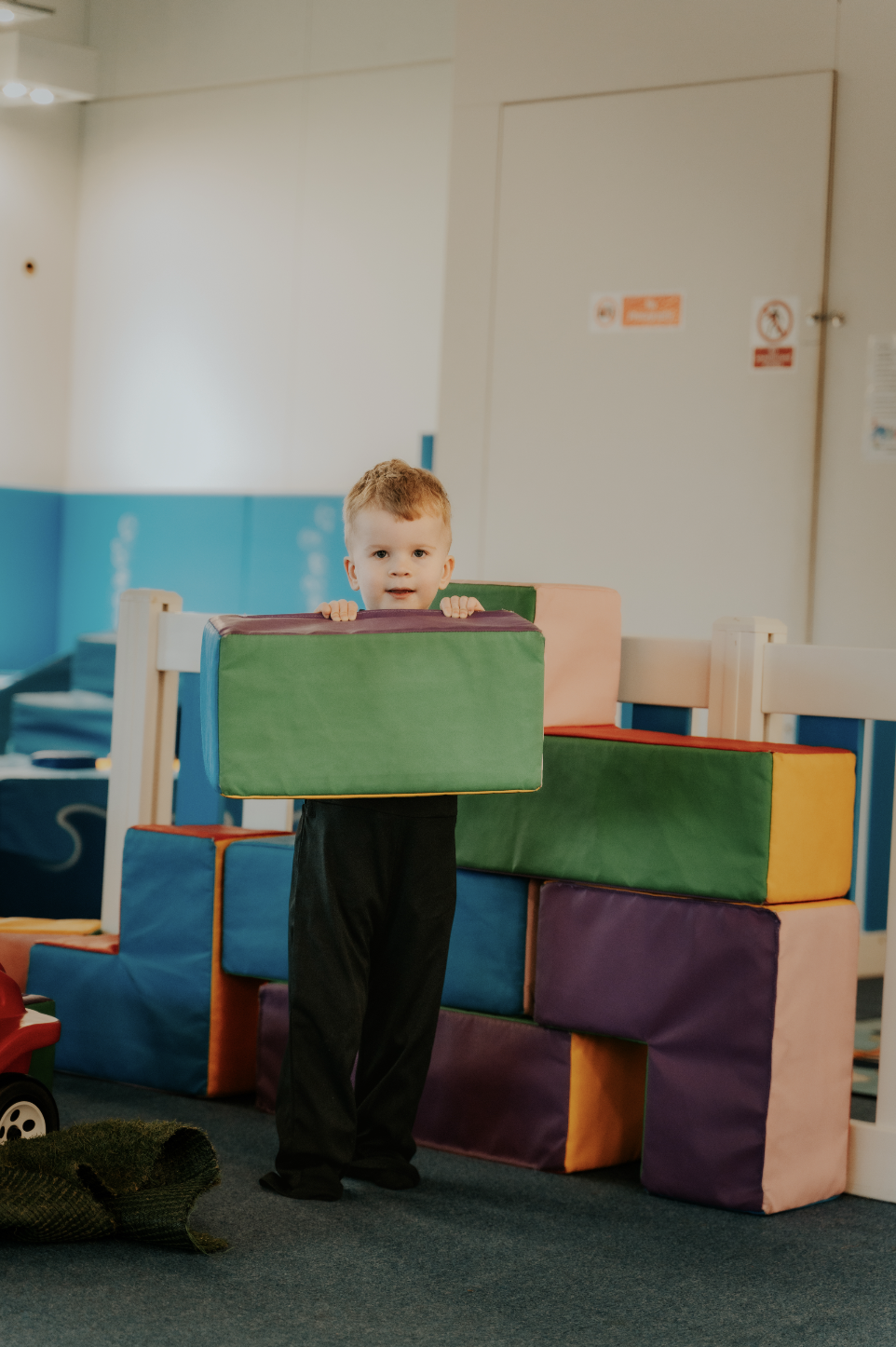 A young boy standing among large colorful foam blocks in a play area at a gymnastics or play center.