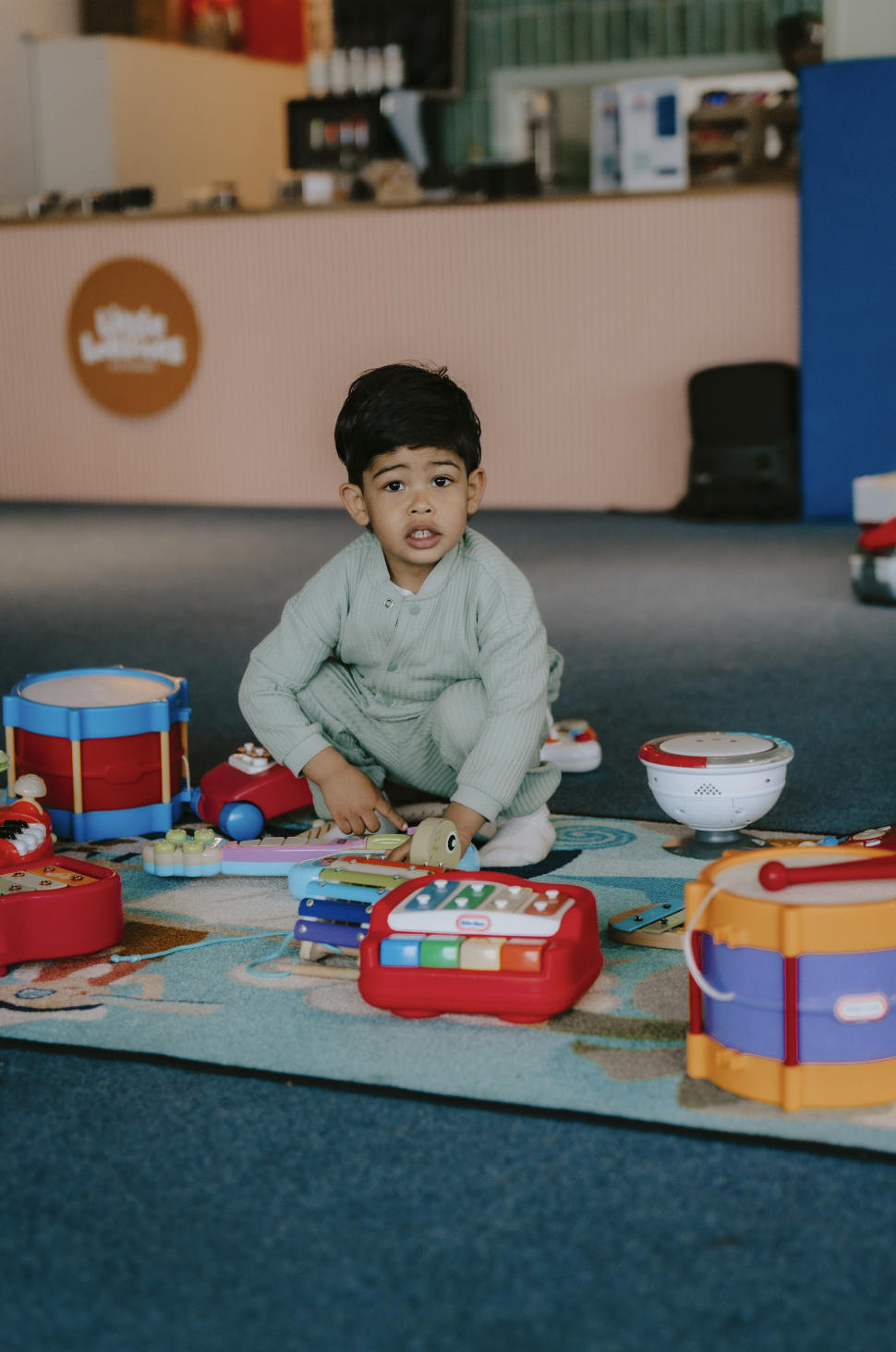 A young boy sitting on the floor with various colorful toy musical instruments around him in a play area.