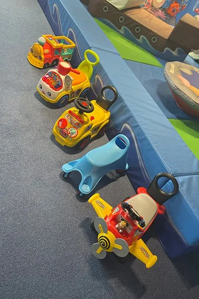 A row of colorful children's ride-on toy cars and a plastic whale among other toys at a play area.
