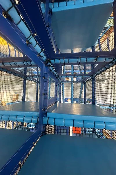 Inside view of a blue indoor playground climbing structure with platforms, slides, and safety netting.