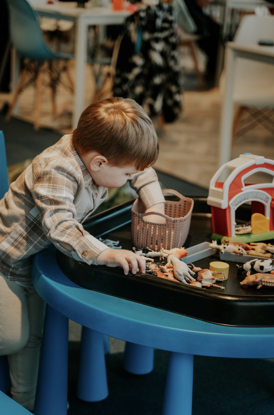 A young boy playing with toy animals on a black table at a daycare or play area.