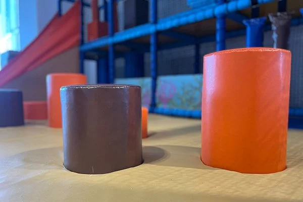 Two cylindrical objects, one brown and one orange, placed on a wooden surface in an indoor setting.