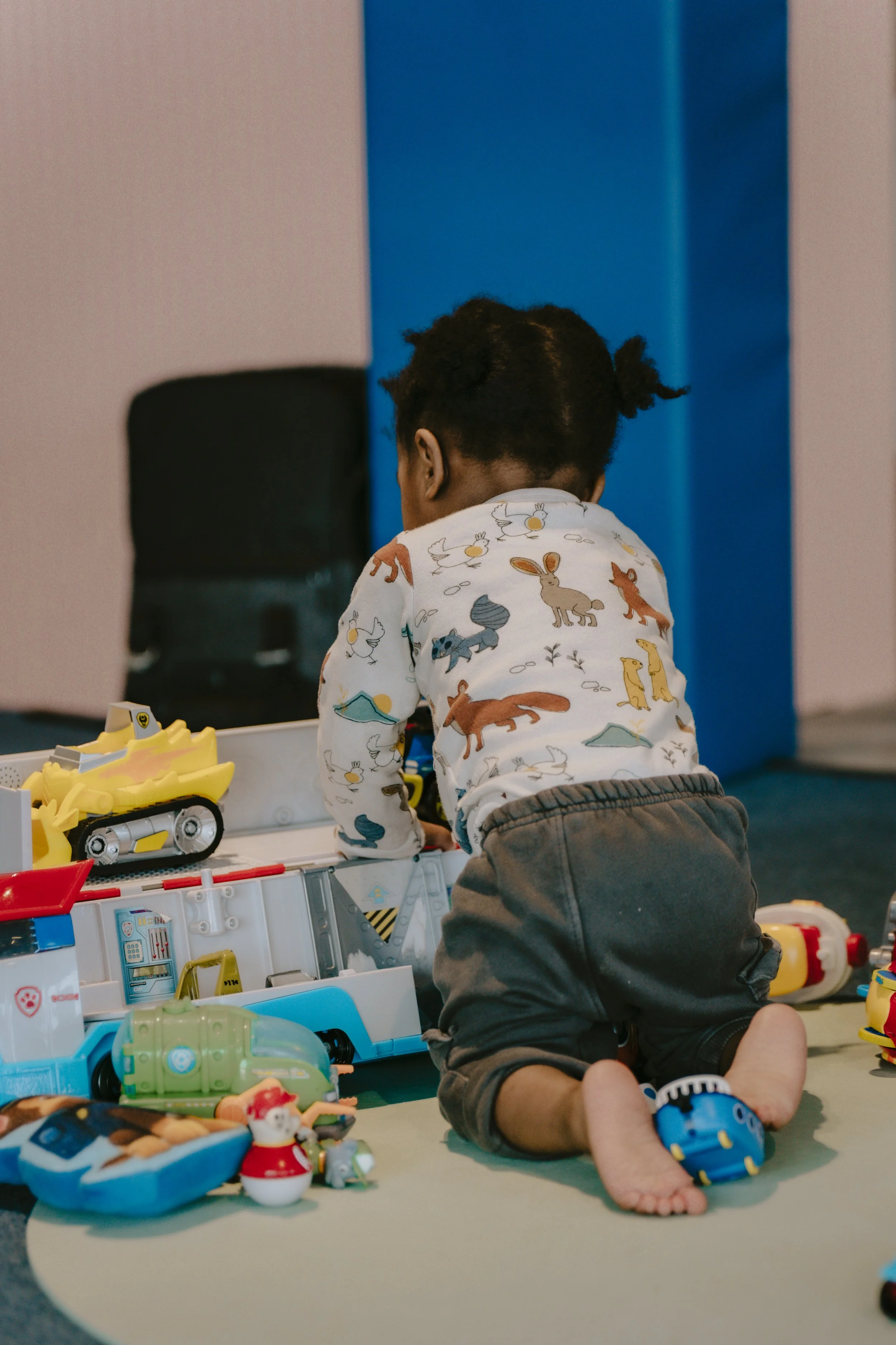 Young child with curly hair wearing a long-sleeve shirt with animal prints, playing with toys on a table.