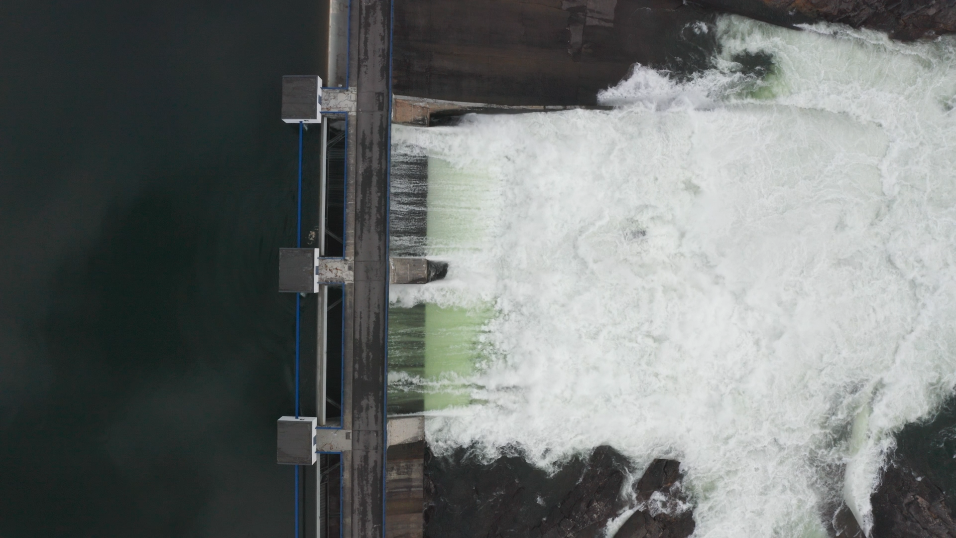 A dam releasing water through spillways with a concrete structure and water flowing forcefully.