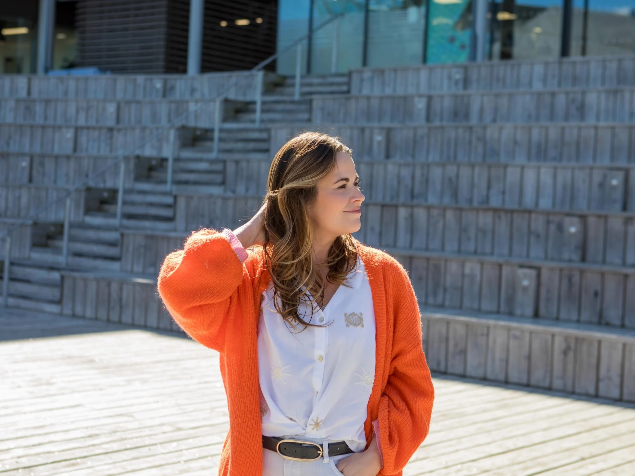 Hayley Buchan Teen Resilience Coach with wavy brown hair wearing an orange cardigan and white shirt, standing outside near modern buildings with large glass windows at Stage@TheDock in Hulll.