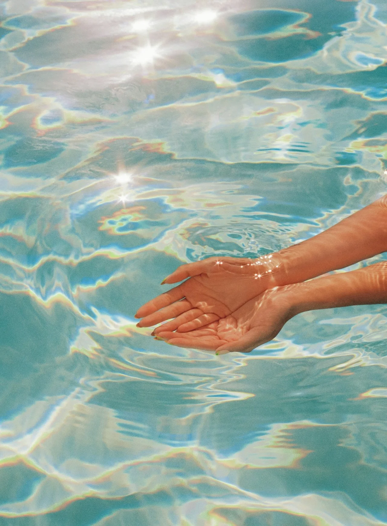 Close-up of a person's two hands gently clasped in a pond with clear, shimmering water reflecting sunlight and creating colorful patterns.