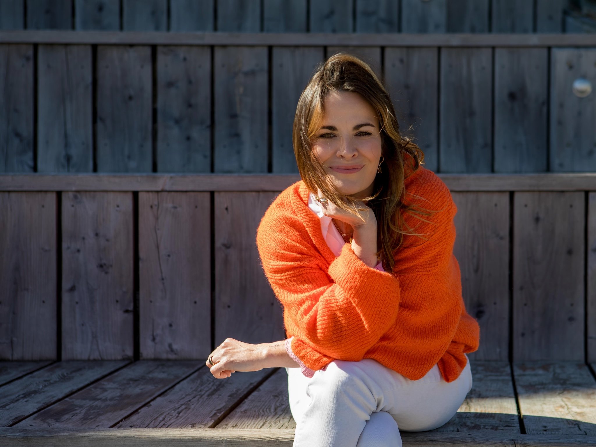 Hayley Buchan Teen Resilience Coach, brown hair sitting outdoors at Stage@TheDock in Hull, wearing an orange sweater and smiling at the camera.
