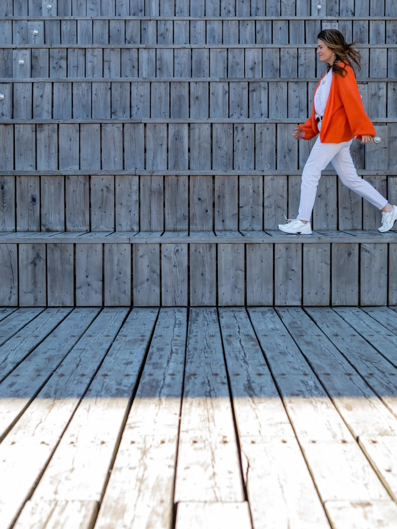 Hayley Buchan Teen Resilience Coach, walking on steps at Stage@TheDock in Hull, wearing a bright orange cardigan and white trousers.