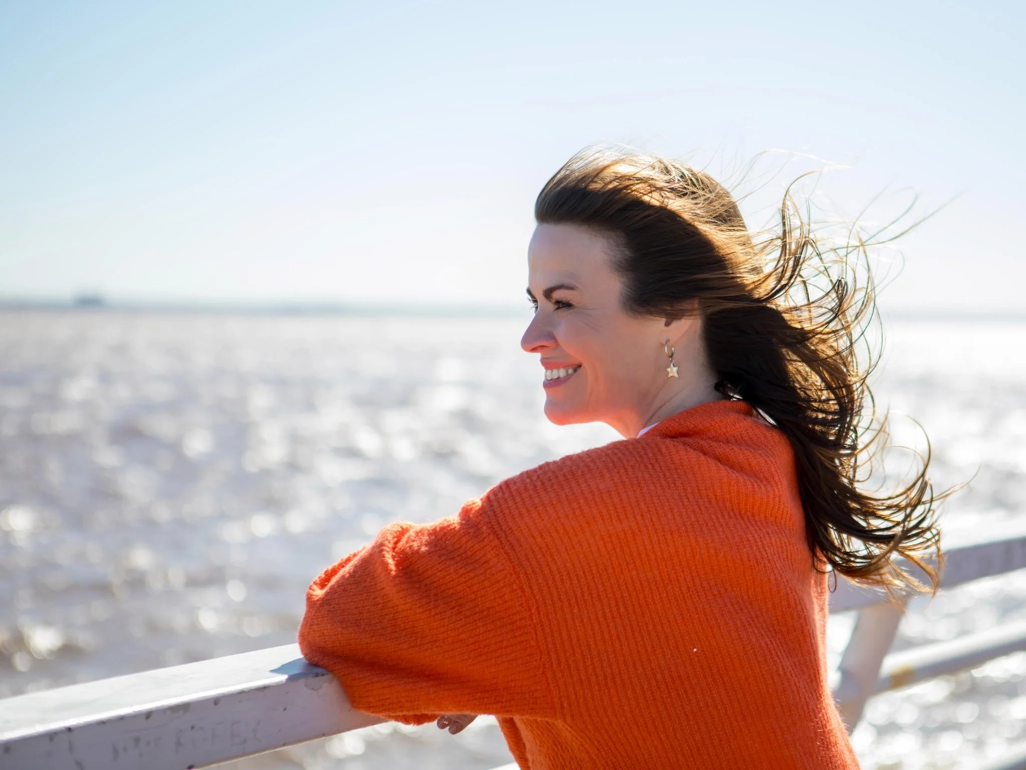 Hayley Buchan Teen Resilience Coach smiling with long hair wearing a star-shaped earring and an orange cardigan enjoying the outdoors with wind blowing her hair on the marina in Hull, Humber Street, Fruit Market.
