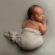 A sleeping newborn baby curled up on a soft surface, wrapped in a light cloth.