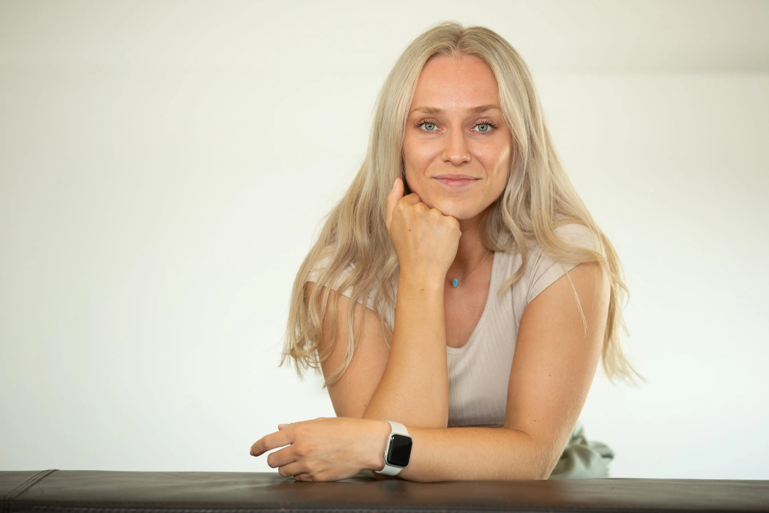 Eine blonde Frau mit blauen Augen, sitzt an einem Tisch und schaut freundlich in die Kamera.
