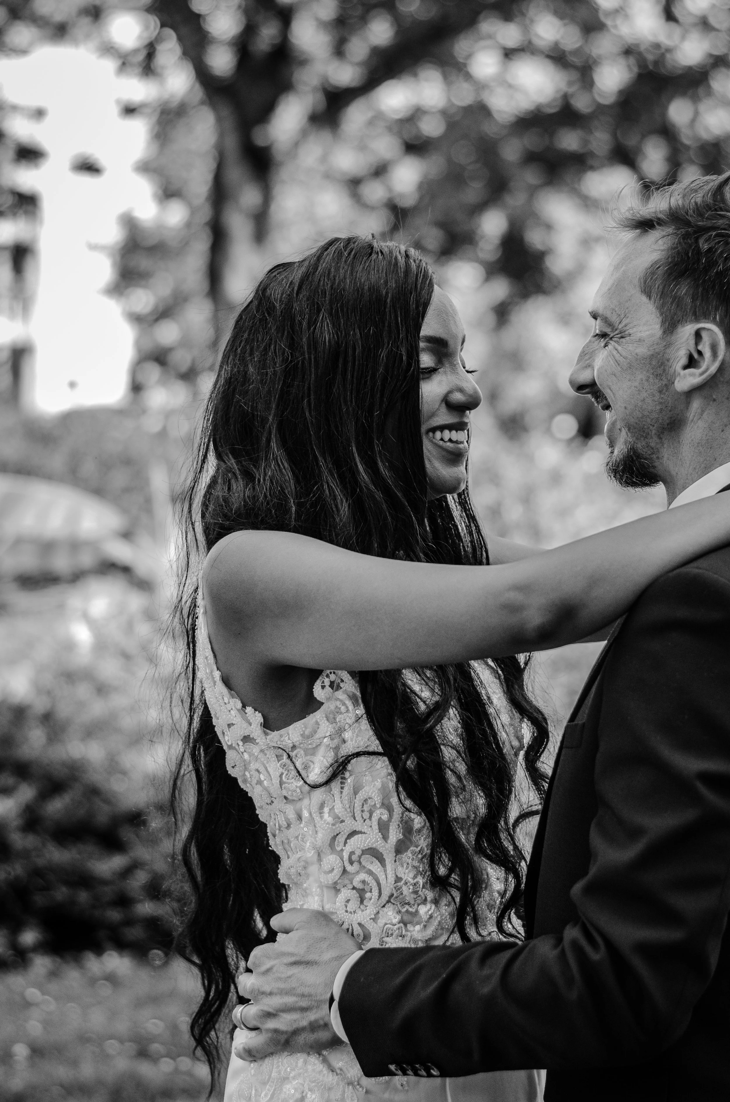 Ein verliebtes Brautpaar, beide lächelnd, miteinander tanzend im Freien, im Hintergrund Bäume, schwarz-weiß Fotografie.