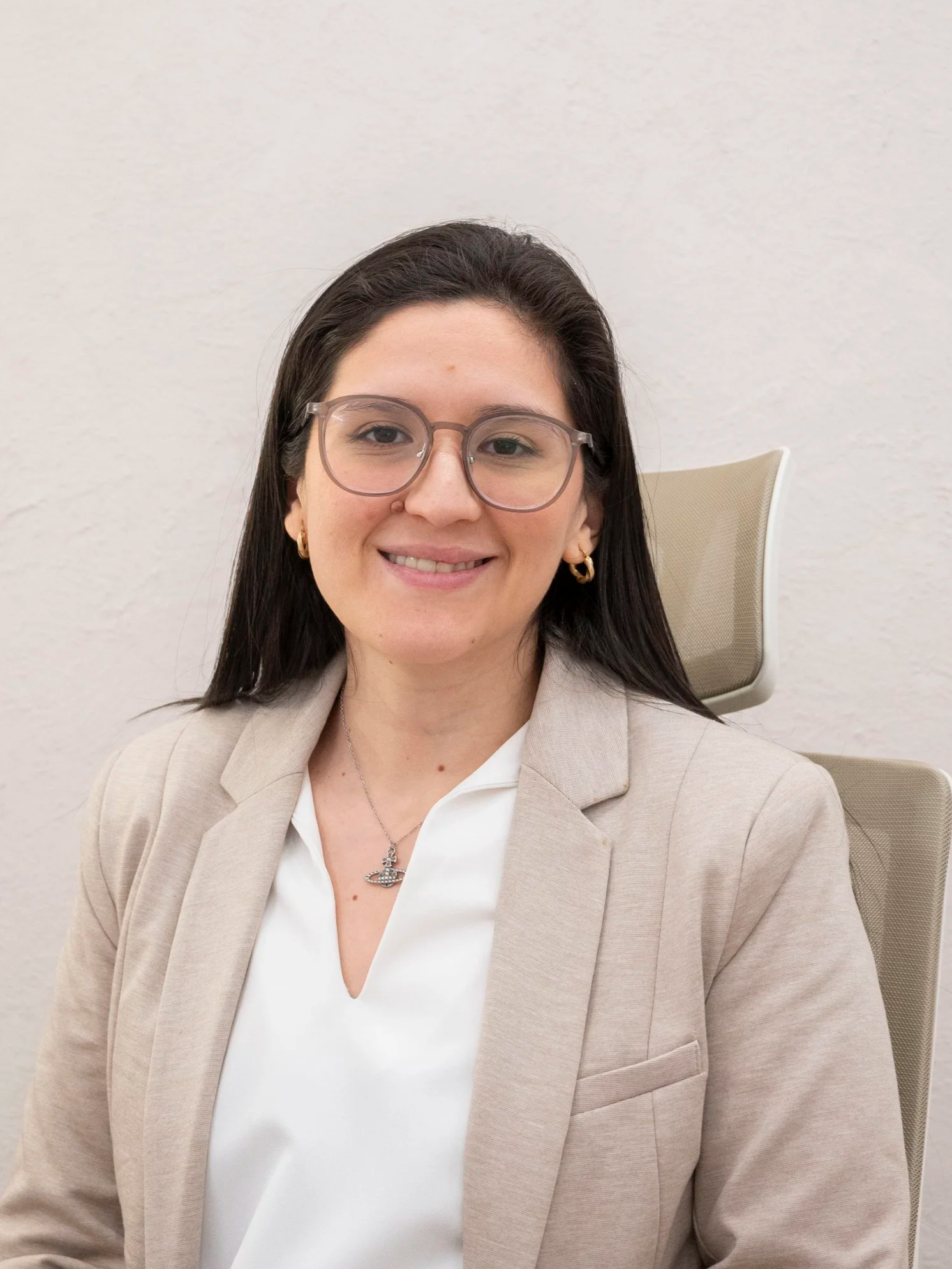 Mujer con gafas y cabello oscuro sentado en una silla oficina con fondo blanco