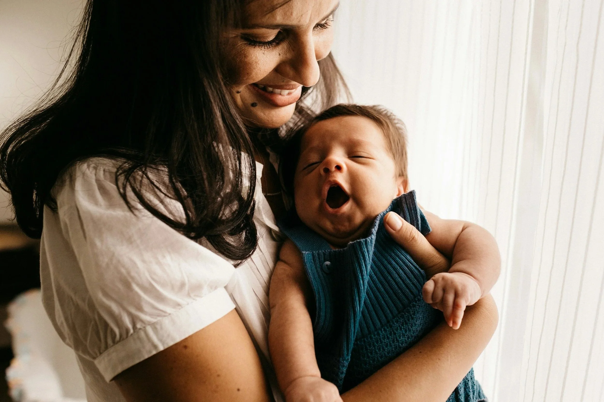 A woman holding a yawning baby in her arms.