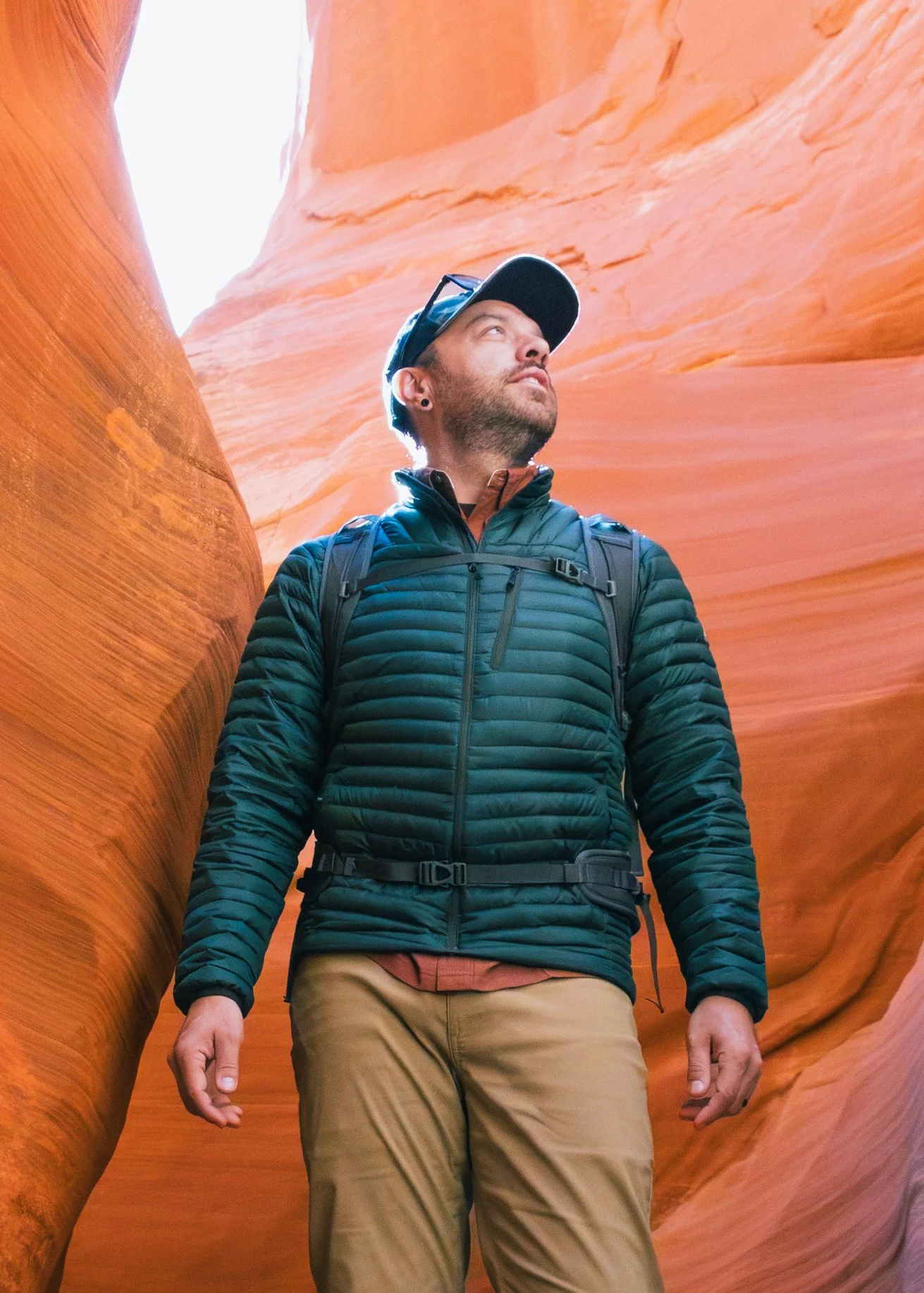 A man wearing outdoor gear exploring a narrow slot canyon with smooth, orange sandstone walls.