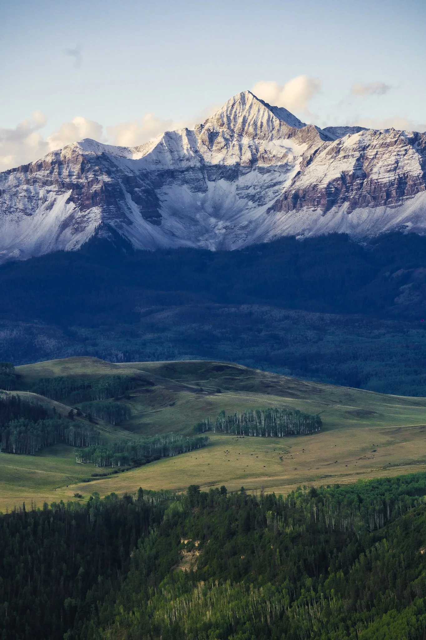 A scenic landscape of snow-capped mountains with a green rolling hill at the foreground.