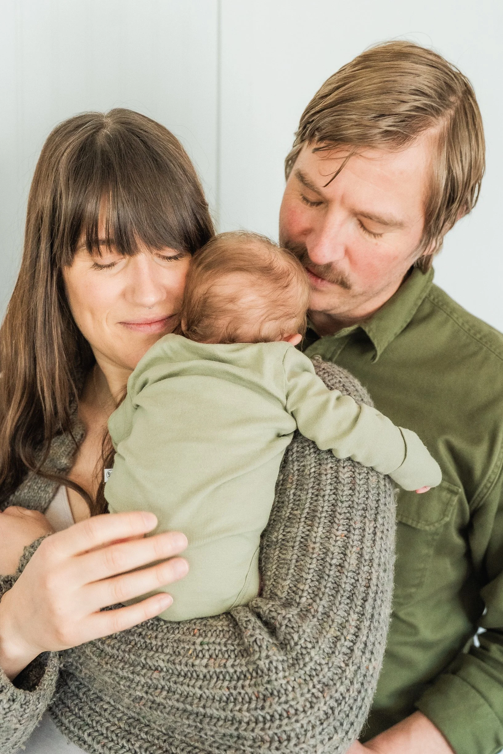 A couple holding a baby, both with eyes closed, in a tender embrace.