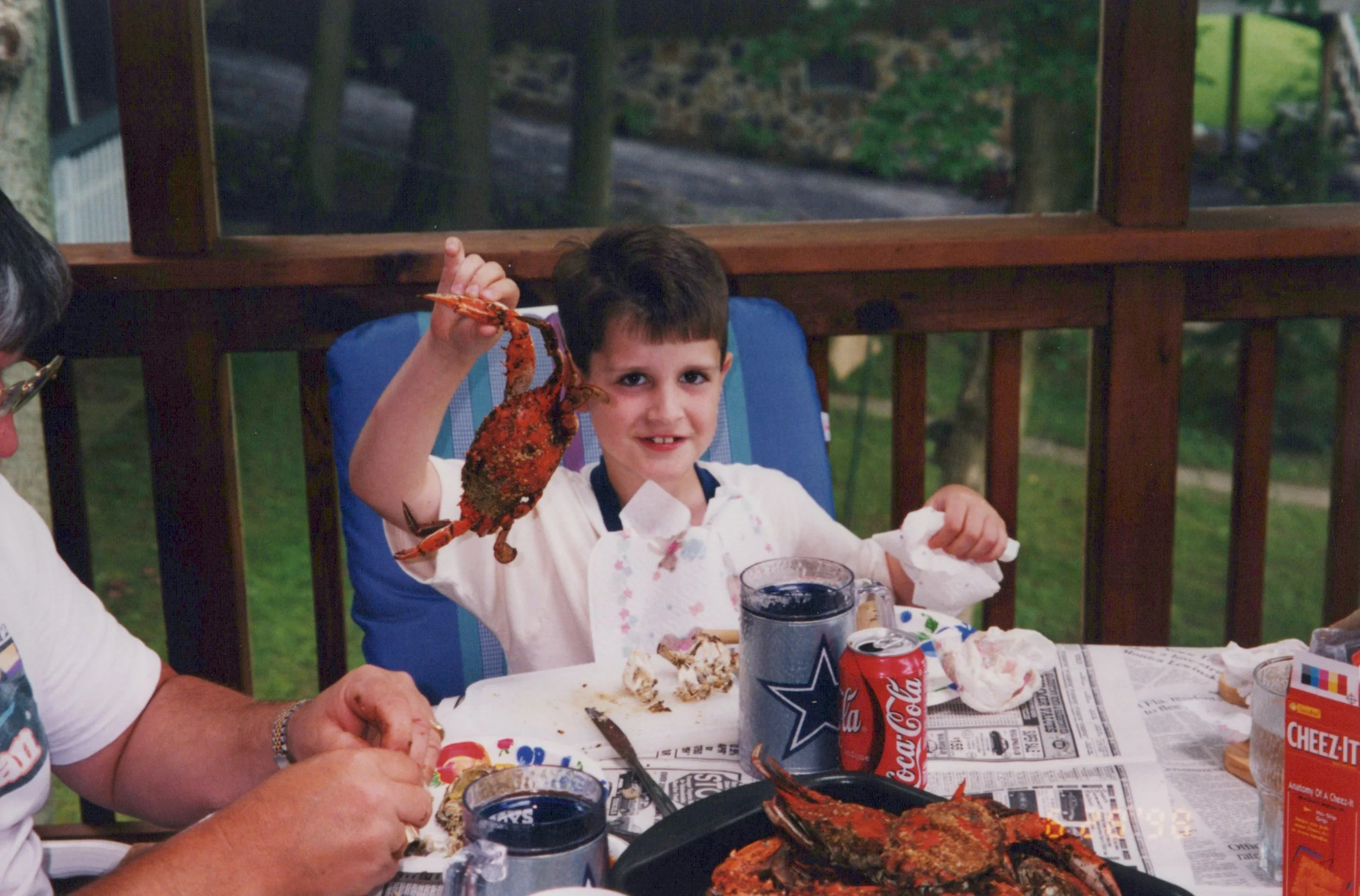 A vintage photo of Craig when he was a child holding up a Maryland Blue Crab at a picnic table along the Potomac River.